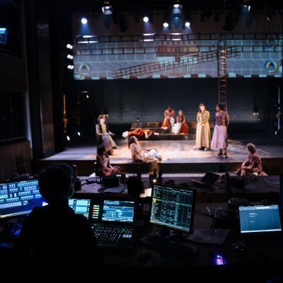 Lighting student working at a lighting desk during a technical rehearsal with the actors on stage